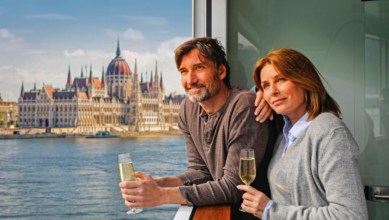 Two guests holding champagne flutes looking out at the views of Budapest from the ship