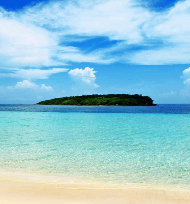 View of a small island in the Caribbean from a beach, surrounded by crystal blue water